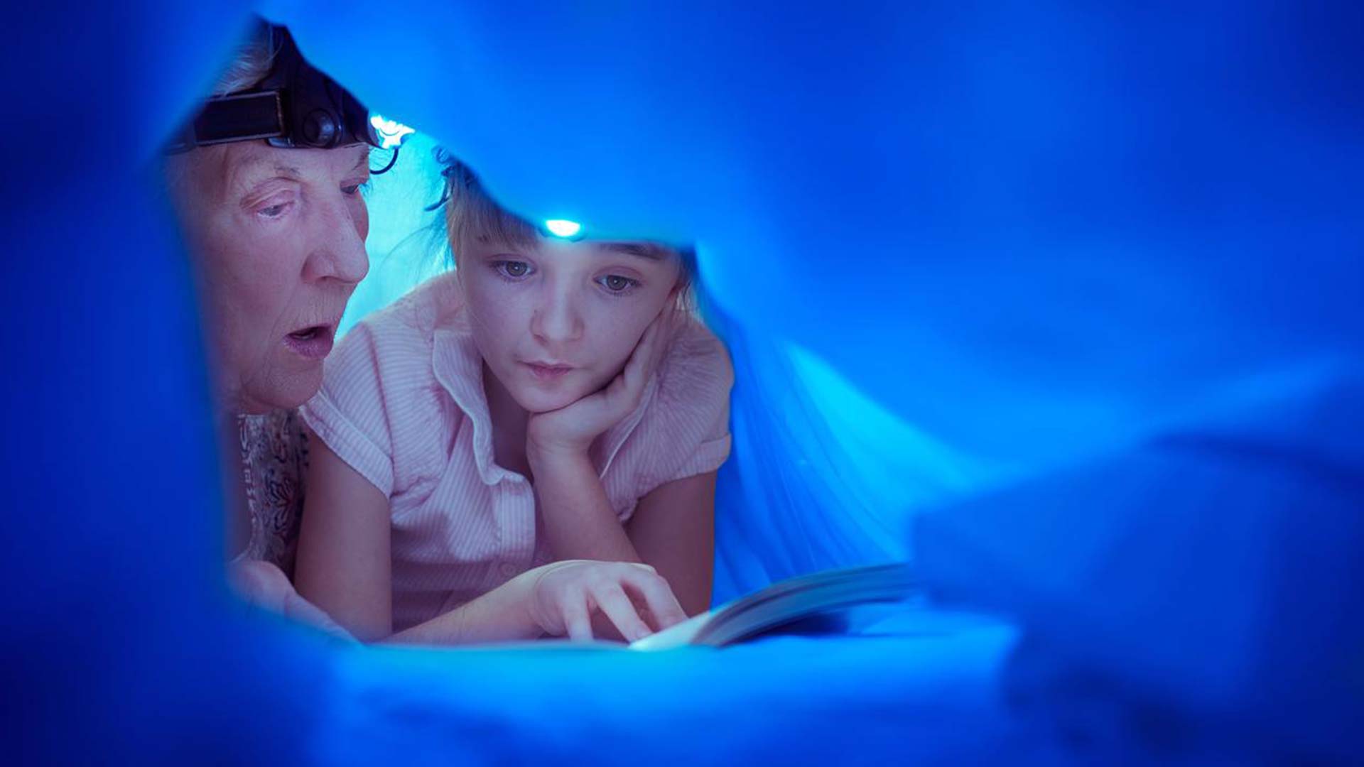 Primer plano de abuela y nieta leyendo a oscuras con una linterna.